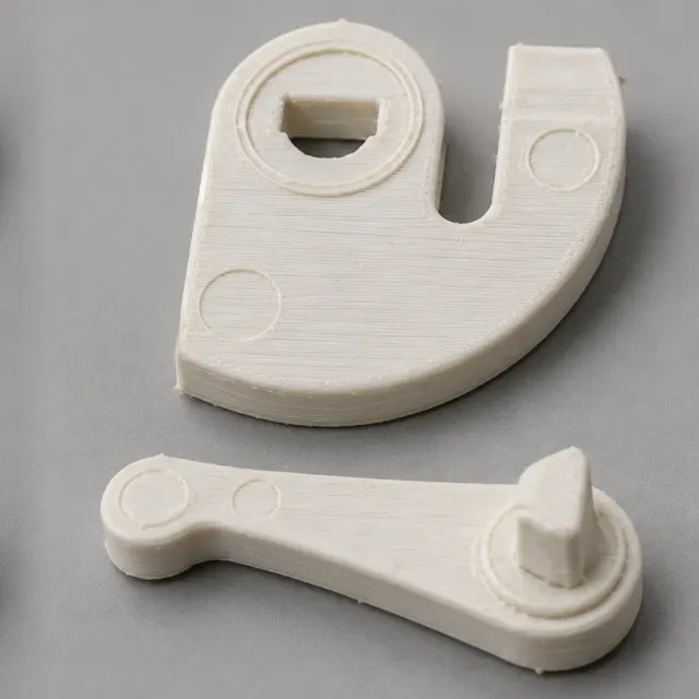 Zwei Kunststoffteile einer Mechanik: eine Platte mit Aussparung für eine Achse und ein Hebel mit Zapfen, im 3D-Druck nachgefertigt